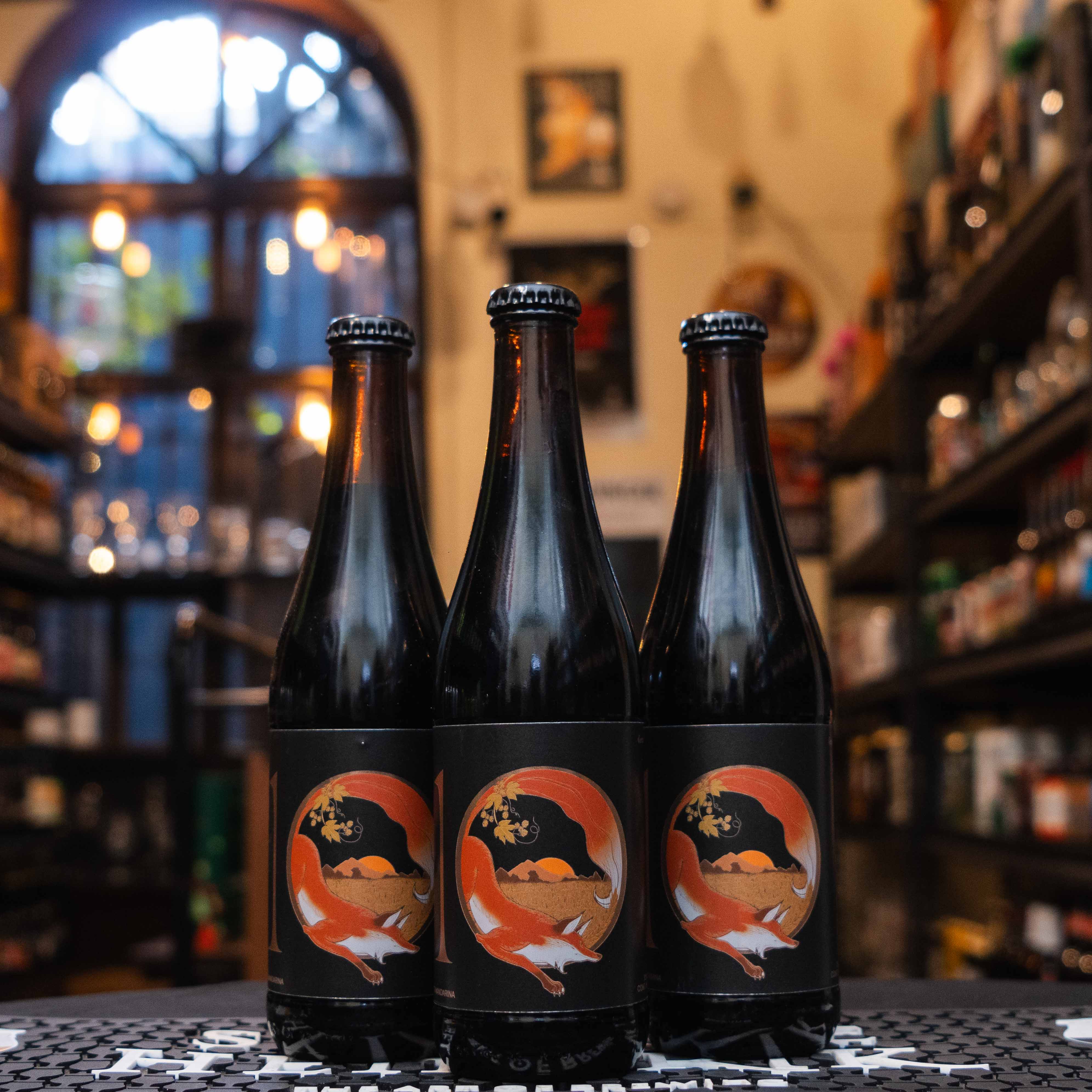 Botella de La Zorra 10 Aniversario Imperial Stout Cacao Mandarina, una edición especial de Cervecería Zorra. La etiqueta negra muestra una ilustración de una zorra roja con detalles dorados y cítricos. Con un ABV de 10% (verificar), combina notas de cacao, malta tostada y un toque fresco de mandarina. Ideal para maridar con postres de chocolate y tartas cítricas. Su diseño celebra 10 años de tradición cervecera.