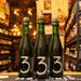 Botella de 3 Fonteinen Oude Geuze, una Lambic tradicional belga. La etiqueta minimalista muestra un gran número '3' blanco sobre fondo verde oscuro. La botella de 75 cl es de vidrio verde, con un corcho que lleva un sello del año '2021'. ABV de 6%, ofrece notas ácidas de manzana verde, limón y roble. Ideal para maridar con quesos añejos y mariscos. El diseño refleja la autenticidad y tradición de la cerveza belga.