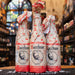 Botella de Bacchus Kriek, una Fruit Beer de Brouwerij Van Honsebrouck, Bélgica. Con un ABV de 5.8%, ofrece un color rojo profundo y aromas de cerezas maduras con notas de madera. Sabor agridulce equilibrado, con un toque final amargo. Ideal para maridar con postres de chocolate oscuro, platos de pato y quesos fuertes. Presentación en botella envuelta en papel distintivo.