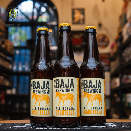  Cabotella Blonde Ale de Baja Brewing Company, mostrando su etiqueta distintiva con el logo de la cervecería y un diseño que evoca la esencia de Los Cabos. La cerveza, de color dorado brillante, se presenta en un vaso con una espuma blanca y ligera.