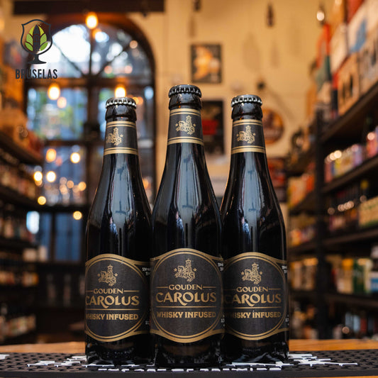 Botella de Gouden Carolus Whisky Infused, una Belgian Strong Ale con infusión de whisky, elaborada por Brouwerij Het Anker. La etiqueta es negra con detalles dorados, y el nombre en letras doradas. ABV de 11.7%, con sabores complejos de malta tostada, vainilla, roble y chocolate. Ideal para maridar con quesos fuertes, carnes asadas y postres de chocolate. El diseño refleja la sofisticación y fuerza de esta cerveza.