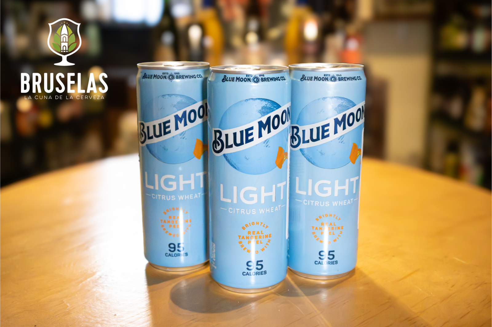 3 cervezas en presentación de lata de la cerveza Blue Moon, en su presentación Light con sabor citrus wheat sobre una mesa de madera