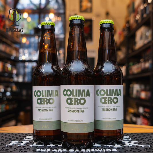 Botella de Colima Cero Session IPA, una cerveza sin alcohol de la Cervecería de Colima. La etiqueta es blanca con detalles verdes y letras modernas. Con menos de 0.5% ABV, ofrece notas cítricas, frutales y un amargor suave en un cuerpo ligero. Ideal para maridar con tacos de pescado, ensaladas frescas y sushi. Su diseño refleja frescura y modernidad.