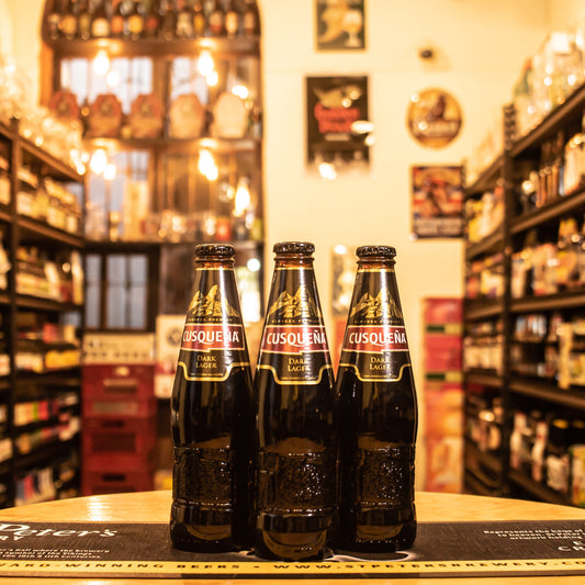 Botella de Cusqueña Negra, una Dark Lager de origen peruano elaborada por la Unión de Cervecerías Peruanas Backus y Johnston. Con un ABV de 5.6%, esta cerveza destaca por sus aromas a chocolate, café y caramelo. Su sabor es intenso, con un equilibrio entre notas dulces y amargas. Ideal para maridar con postres de chocolate, carnes asadas y quesos fuertes. Presentación en botella de 330 ml, perfecta para quienes disfrutan de cervezas con cuerpo robusto y sabores complejos.