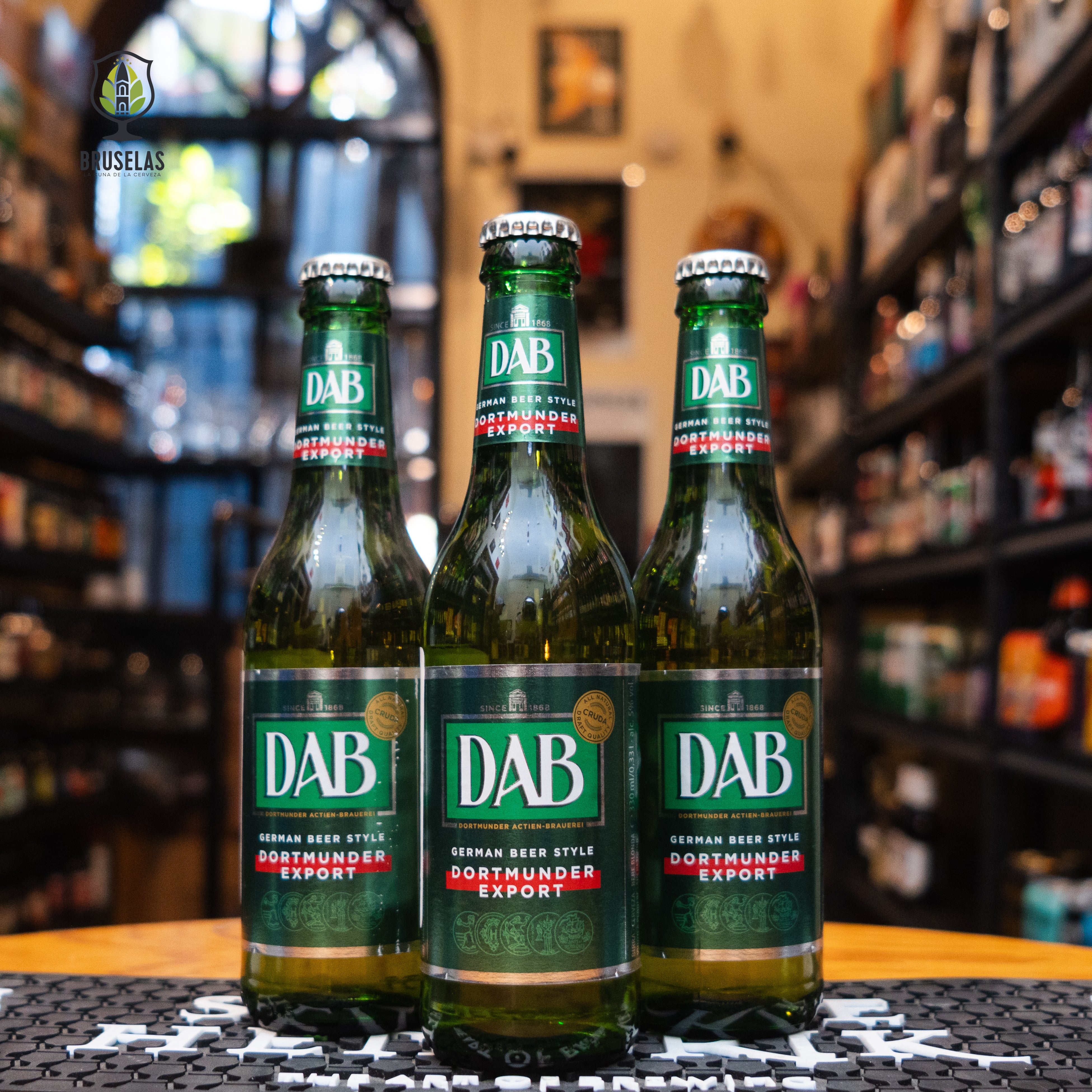 Botella de DAB Export de 330 ml, una lager alemana clásica elaborada por Dortmunder Actien Brauerei. Con un ABV de 5.0%, esta cerveza presenta un color dorado brillante y una claridad impecable. Su sabor es suave y equilibrado, con sutiles notas de malta y un ligero amargor al final, ofreciendo una experiencia refrescante. Ideal para maridar con ensaladas, pescados y carnes blancas, es perfecta para quienes buscan una cerveza ligera y fácil de beber.