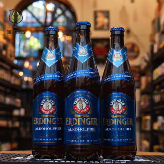 Botella de Erdinger Weissbier Alkoholfrei, una cerveza de trigo sin alcohol de Erdinger Weissbräu, Bavaria. Con menos de 0.5% ABV, destaca por su perfil isotónico, ideal para rehidratación tras el ejercicio. Su sabor pleno y refrescante emula a las cervezas con alcohol, con notas de malta especiada, caramelo y un toque frutal. Es ligera, con un suave amargor y acidez, perfecta para acompañar ensaladas, pescados o disfrutar sola.