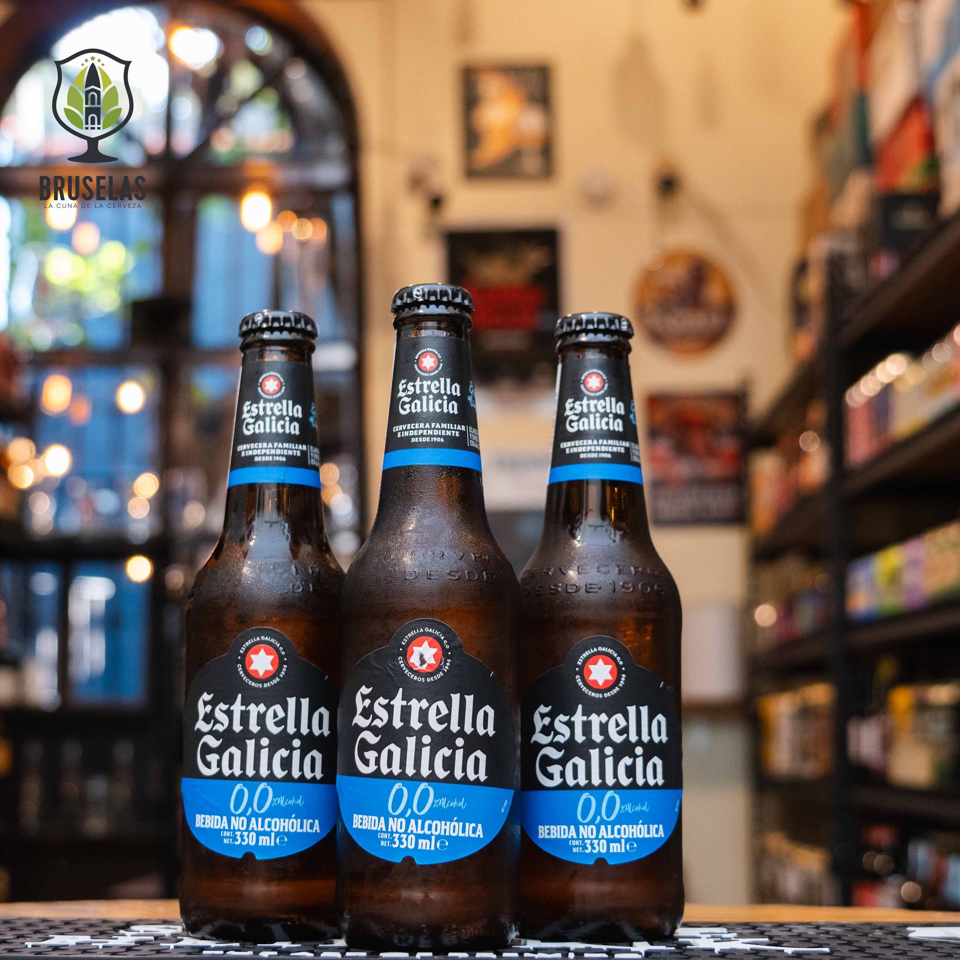 Botella de Estrella de Galicia 0.0, una lager sin alcohol de Hijos de Rivera, S.A. Con un color dorado brillante y un ABV de 0.0%, se elabora mediante un proceso de "fermentación interrumpida", manteniendo las características de una cerveza tradicional. Ofrece aromas de malta y cereales, con sutiles notas florales y de lúpulo. Su sabor es suave, con una dulzura ligera y un final refrescante y amargo. Ideal para maridar con quesos frescos, ensaladas cítricas, mariscos y pescados blancos.