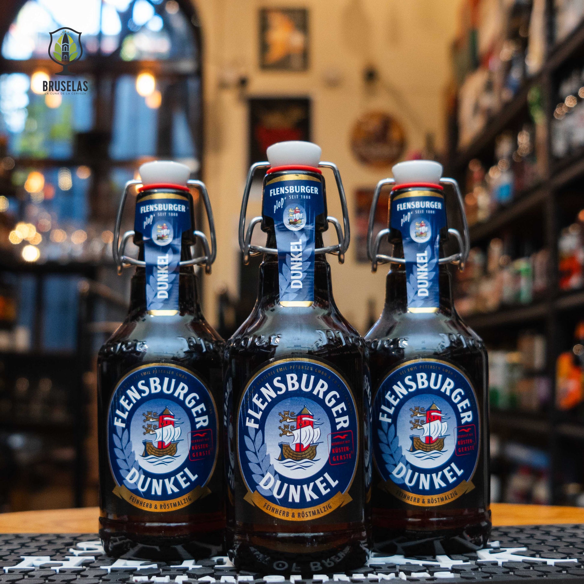 Botella de Flensburger Dunkel, una Dunkel alemana de 4.8% ABV. Su etiqueta azul marino y tapón mecánico reflejan su carácter clásico. Ideal para acompañar embutidos, carnes asadas y quesos maduros.