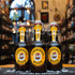 Botella de Flensburger Weizen, una Hefeweizen alemana de 5.1% ABV. Su etiqueta amarilla con el icónico barco y su tapón mecánico resaltan su tradición cervecera. Ideal para acompañar salchichas alemanas, pretzels y quesos suaves.