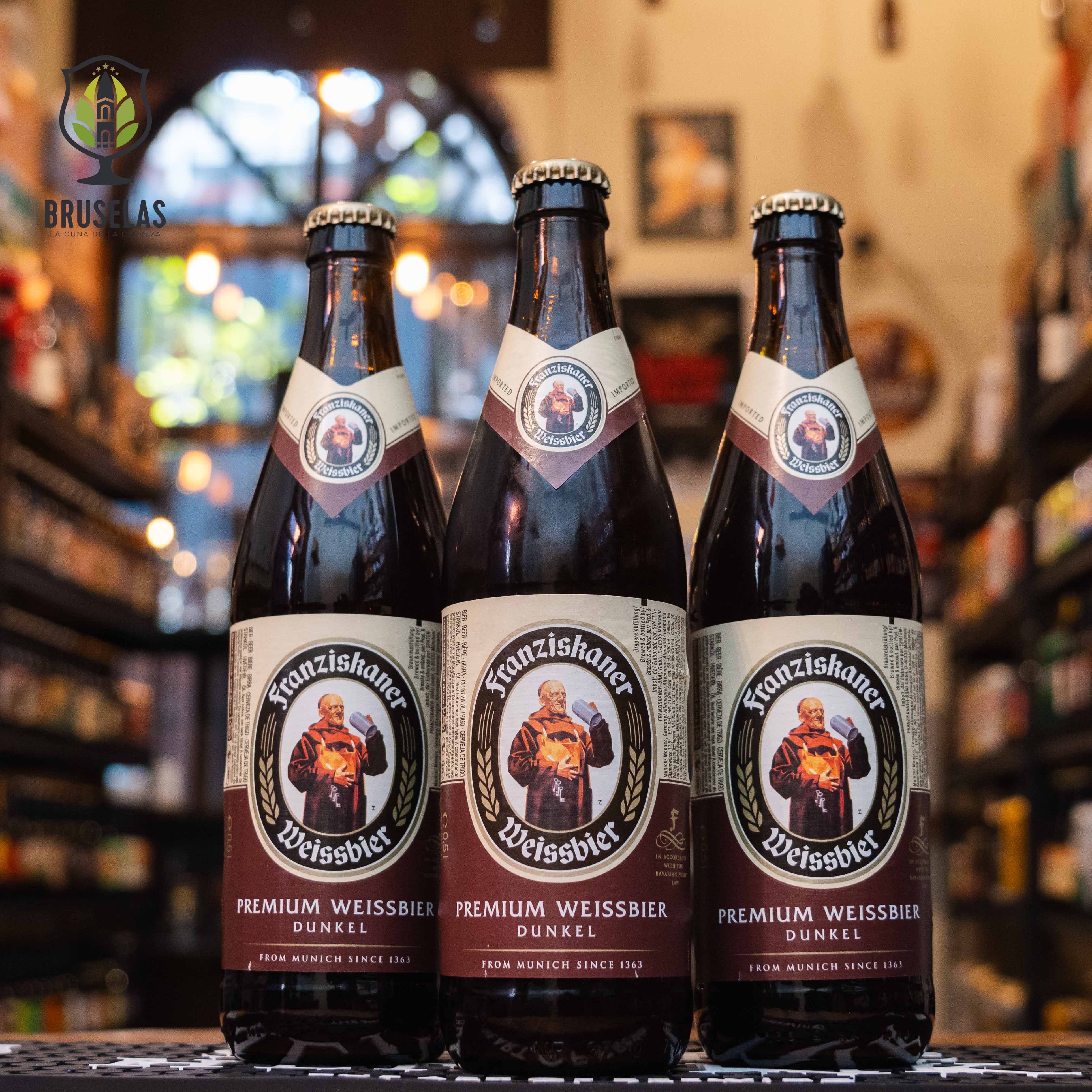 Botella de Franziskaner Hefe-Weissbier Dunkel, una Dunkelweizen de la cervecería Spaten-Franziskaner-Bräu GmbH, elaborada en Baviera, Alemania. La etiqueta presenta el icónico monje Franziskaner sobre un fondo marrón oscuro, con detalles dorados y crema. Con un ABV de 5.0%, ofrece aromas de pan fresco, nueces y caramelo, y un sabor maltoso con notas de plátano, clavo y caramelo. Ideal para maridar con carnes oscuras, platos de caza o postres ricos.