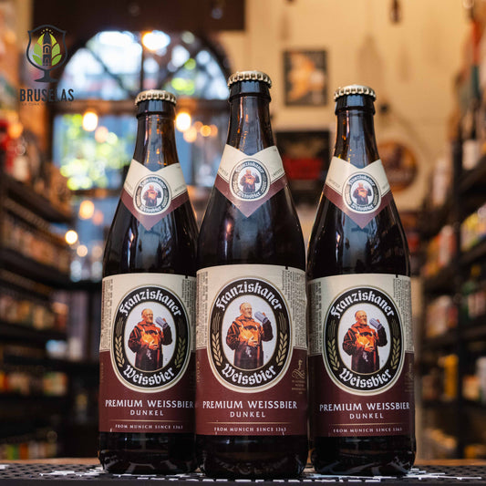 Botella de Franziskaner Hefe-Weissbier Dunkel, una Dunkelweizen de la cervecería Spaten-Franziskaner-Bräu GmbH, elaborada en Baviera, Alemania. La etiqueta presenta el icónico monje Franziskaner sobre un fondo marrón oscuro, con detalles dorados y crema. Con un ABV de 5.0%, ofrece aromas de pan fresco, nueces y caramelo, y un sabor maltoso con notas de plátano, clavo y caramelo. Ideal para maridar con carnes oscuras, platos de caza o postres ricos.