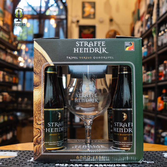 El Giftpack Straffe Hendrik se presenta en una elegante caja verde con detalles dorados, destacando la herencia belga de la marca. Se pueden ver cuatro botellas de 330ml (dos Tripel y dos Quadrupel), junto con una copa oficial con el logo de la marca. El fondo muestra una tienda especializada en cervezas artesanales con iluminación cálida y estanterías bien surtidas. Cambios sujetos a disponibilidad.