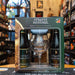 El Giftpack Straffe Hendrik se presenta en una elegante caja verde con detalles dorados, destacando la herencia belga de la marca. Se pueden ver cuatro botellas de 330ml (dos Tripel y dos Quadrupel), junto con una copa oficial con el logo de la marca. El fondo muestra una tienda especializada en cervezas artesanales con iluminación cálida y estanterías bien surtidas. Cambios sujetos a disponibilidad.