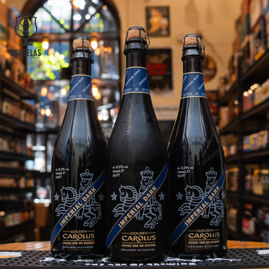 Botella de Gouden Carolus Imperial Dark, una Belgian Strong Dark Ale de Brouwerij Het Anker, con un ABV de 11%. La etiqueta negra y azul muestra un emblema de caballero. Ofrece aromas de malta tostada, caramelo y ciruelas, con sabores de chocolate y frutos secos, y un final cálido. Ideal para maridar con carnes rojas, postres de chocolate y quesos fuertes.