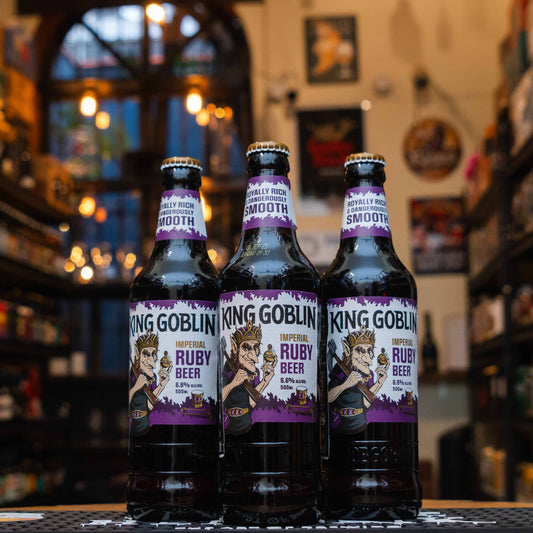 Botella de King Goblin, una Strong Ale de edición especial elaborada por Wychwood Brewery en Witney, Inglaterra. La etiqueta presenta un diseño místico y tonos rubí oscuros. ABV de 6.6%, con aromas a malta rica, frutas oscuras y lúpulos terrosos. Sabor a toffee, pasas, malta tostada y toque de cítricos. Ideal para acompañar platos de caza, quesos fuertes y postres ricos. Refleja un perfil robusto y complejo.