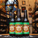 Botella de Insurgente Frida, una Wheat Beer afrutada de Cervecería Insurgente con un ABV de 4.5%, elaborada en Tijuana, México. La etiqueta es colorida con ilustraciones de una sandía y la cara de un perro blanco en el centro. Presenta notas aromáticas de limón y sandía, con un cuerpo suave gracias a la malta de trigo y pilsner. Ideal para acompañar ensaladas y mariscos frescos.