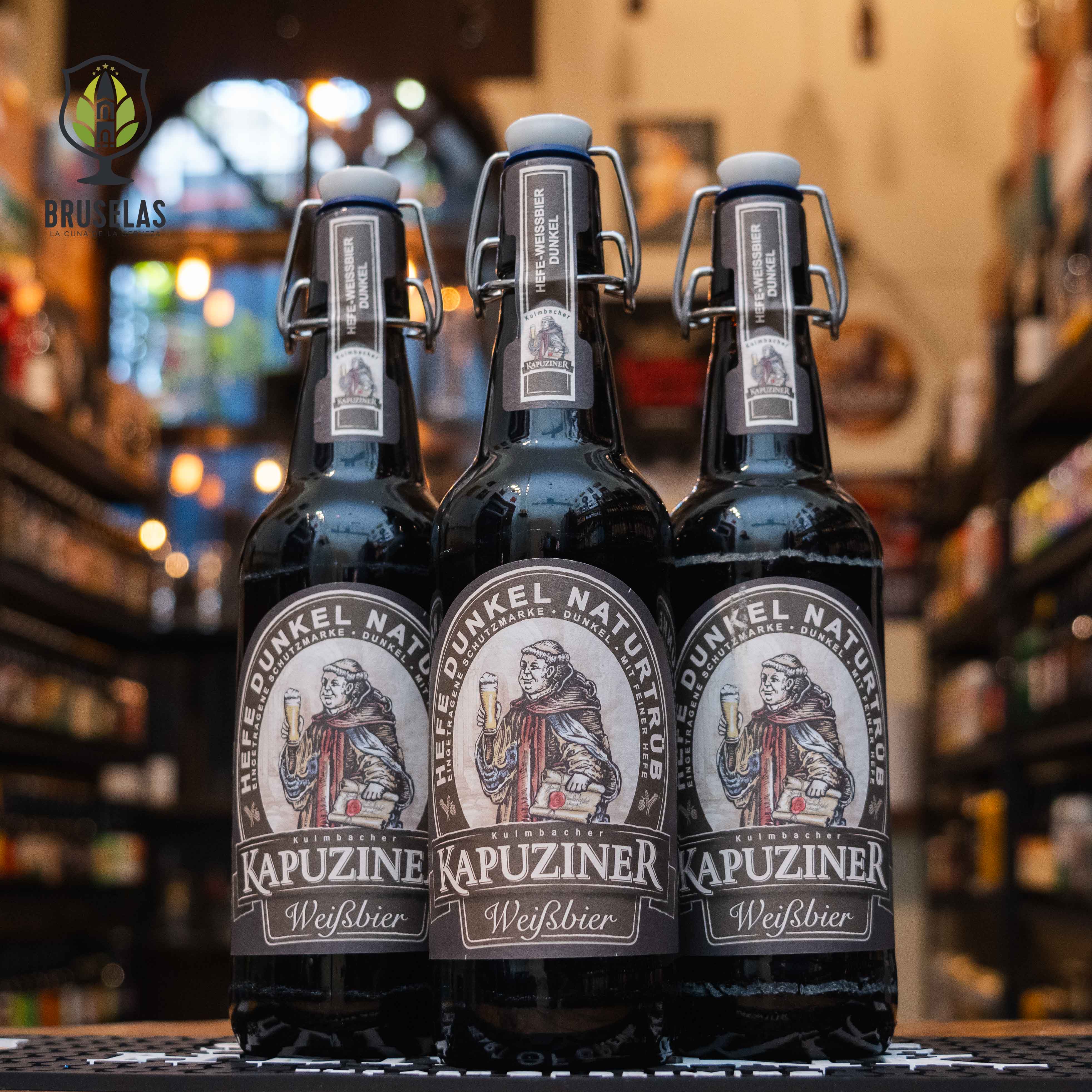 Botella de Kapuziner Schwarzbier, una cerveza oscura estilo Schwarzbier de la cervecería alemana Kapuziner. Con un ABV de 5.4%, presenta un color marrón profundo y espuma cremosa beige. Destacan sus aromas a malta tostada, caramelo y café. Su sabor es complejo, con un suave amargor y un final especiado. Ideal para maridar con carnes asadas, platos de caza o postres de chocolate como brownies.