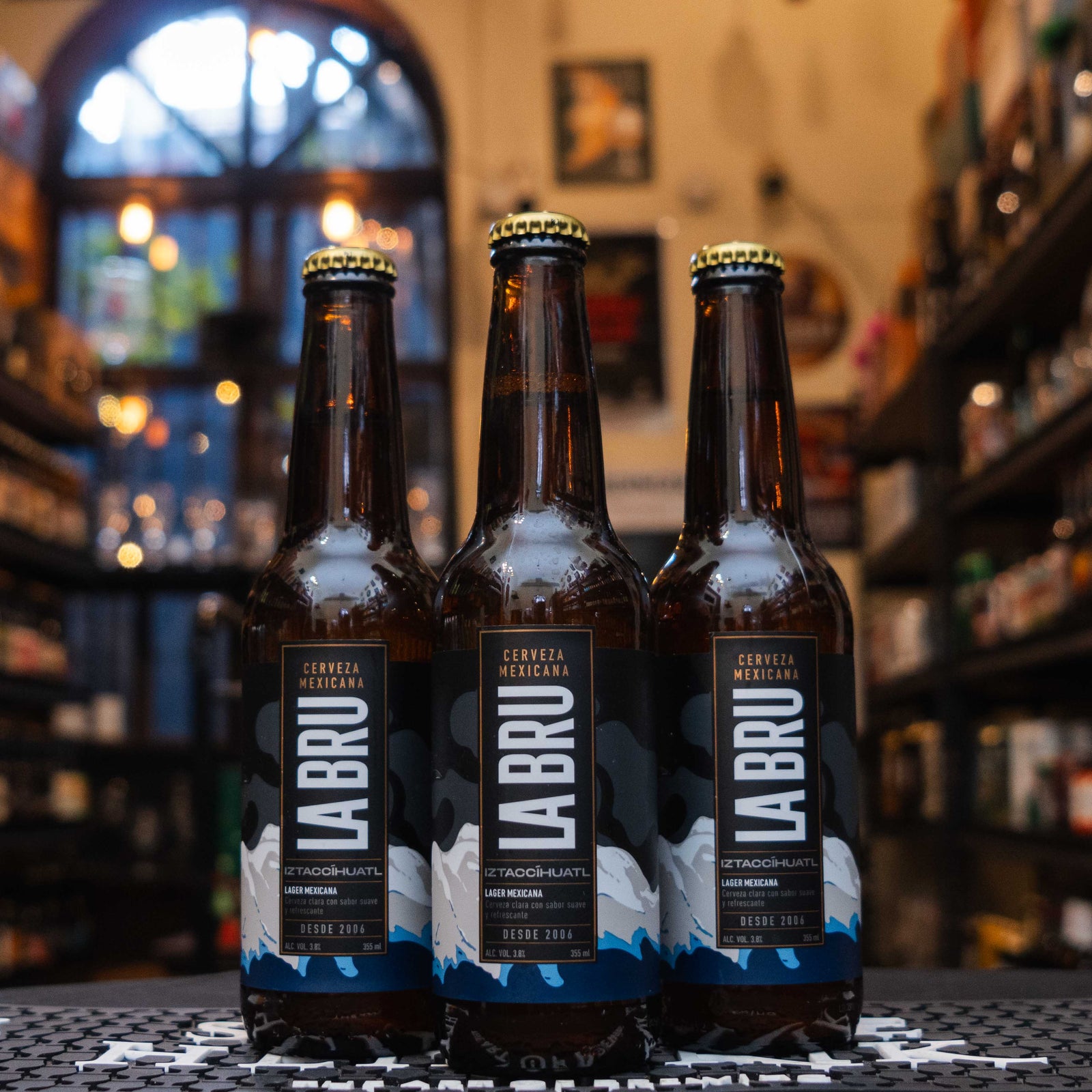 Botella de La Bru Iztaccíhuatl, una lager mexicana de la cervecería artesanal La Bru. La etiqueta tiene un diseño negro con tonos blancos y azules, representando montañas, y letras blancas en fuente moderna. Con un ABV de 3.8%, ofrece un perfil fresco y balanceado. Ideal para acompañar platillos ligeros como ensaladas y pescados. Su diseño celebra la tradición y paisajes mexicanos.