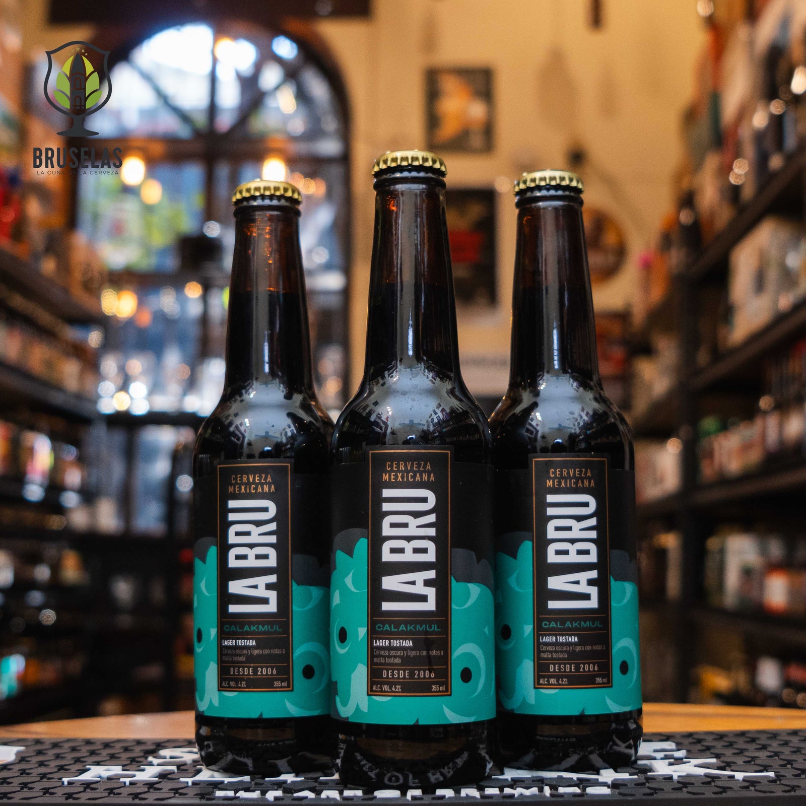 Botella de La Bru Calakmul, una Dark Lager de la cervecería mexicana La Bru. La etiqueta es negra con detalles en verde turquesa y letras blancas modernas, inspirada en la cultura maya. Con un ABV de 4.2%, ofrece notas de maltas tostadas, caramelo, café y chocolate, con un amargor moderado. Ideal para maridar con carnes asadas, enchiladas y postres de chocolate. Su diseño celebra la majestuosidad de Calakmul.