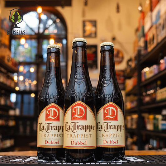 Botella de La Trappe Dubbel, una cerveza de estilo Belgian Dubbel elaborada por Brouwerij De Koningshoeven en los Países Bajos. La etiqueta presenta tonos crema y rojo, con el logotipo de la cervecería trapense. Con un ABV de 7.0%, su sabor complejo incluye maltas tostadas, caramelo y frutas oscuras como ciruelas. Ideal para acompañar estofados, carnes asadas y quesos fuertes. Presentación en botella de 330 ml.