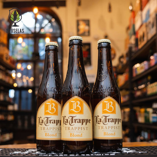 Botella de La Trappe Blond, una cerveza de estilo Belgian Blond Ale elaborada por Brouwerij De Koningshoeven en los Países Bajos. La etiqueta presenta el logotipo distintivo 'LB' en dorado, con detalles en blanco y amarillo, que reflejan su estilo trapense. Con un ABV de 6.5%, esta cerveza ofrece un perfil aromático de notas frutales y especiadas. Ideal para maridar con ensaladas, pescados y quesos suaves. Presentación en botella de 330 ml.