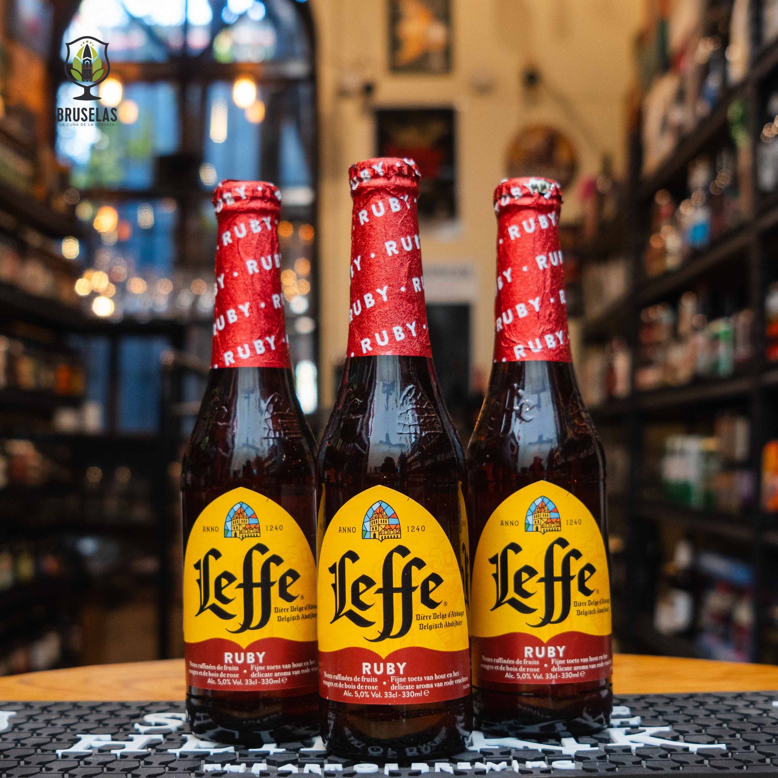 Botella de Leffe Ruby, una cerveza de abadía belga de Abbaye de Leffe. La etiqueta presenta tonos rubí y dorado, reflejando su carácter afrutado. Con 5% ABV, ofrece aromas de frambuesa, fresa y notas especiadas. Ideal para maridar con pescados blancos, jamón serrano y quesos de cabra.