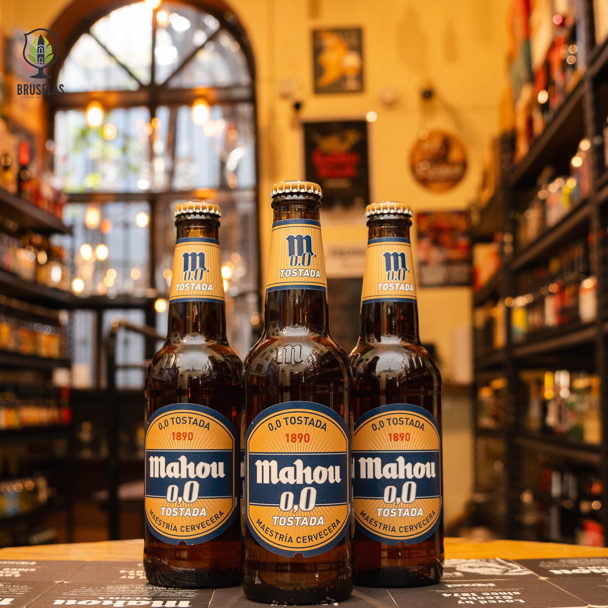 Botella de Mahou 0,0 Clásica, una cerveza sin alcohol de Mahou, con un color dorado brillante y un sabor suave con un amargor ligero. La Mahou 0,0 Tostada se distingue por su color ámbar oscuro, aromas a maltas tostadas y un regusto dulce. Ambas cervezas, con 0.0% ABV, son ideales para maridar con verduras a la parrilla, embutidos de ave y quesos suaves. Reflejan frescura y equilibrio sin alcohol.