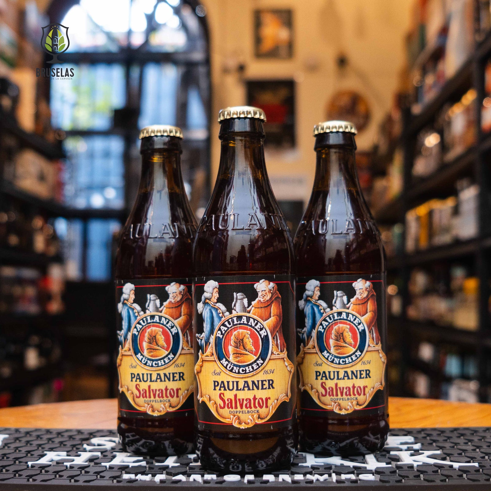  Paulaner Salvator, Doppelbock de 7.9% ABV, con una etiqueta clásica que muestra a dos monjes brindando. Su color ámbar oscuro y su perfil maltoso la convierten en una joya cervecera ideal para disfrutar lentamente.