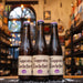 Botella de Trappistes Rochefort Triple Extra, una cerveza estilo Tripel de la Abadía de Notre-Dame de Saint-Rémy en Bélgica. La etiqueta tiene letras góticas negras sobre fondo beige con un emblema morado que indica 'Triple Extra'. ABV de 8.1%, con sabores frutales y especiados, ideal con mariscos, quesos y aves. El diseño refleja la tradición trapense.