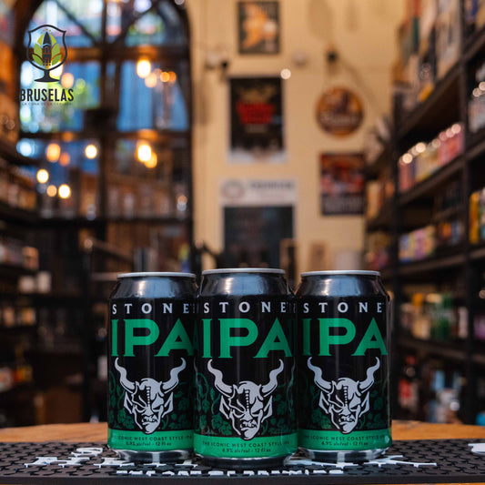 Lata de Stone IPA, una West Coast IPA de Stone Brewing, elaborada en EE.UU. La etiqueta es negra con letras verdes grandes y un logo de gárgola en blanco. Con un ABV de 6.9%, ofrece sabores cítricos, frutas tropicales y pino. Ideal para tacos picantes, pollo al curry y quesos fuertes. El diseño de la lata es moderno y atrevido.