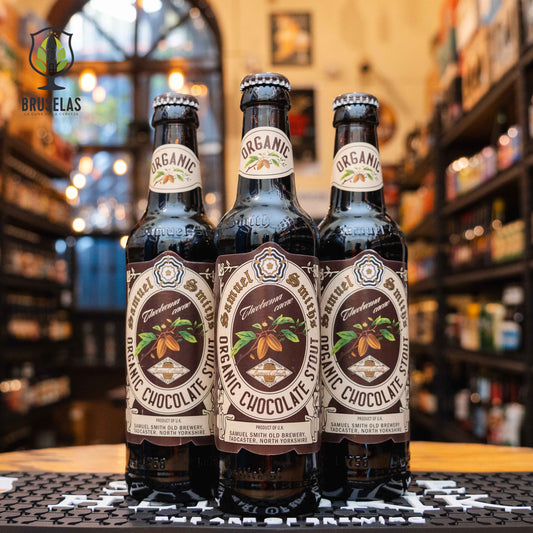 Botella de Samuel Smith Organic Chocolate Stout, una cerveza artesanal estilo stout elaborada en Inglaterra por Samuel Smith Old Brewery. La etiqueta es marrón con detalles de cacao. ABV de 5.0%, con aromas de cacao, vainilla y malta tostada. Sabor dulce y cremoso con notas prominentes de chocolate. Ideal para acompañar postres de chocolate, brownies y helado de vainilla. Diseño clásico y orgánico.