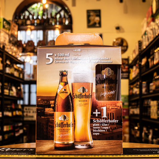 Schöfferhofer Gift Pack, que incluye 5 botellas de Schöfferhofer Hefeweizen 500ml y 1 vaso oficial de la marca. Ubicado sobre una barra en un ambiente cervecero, resaltando su presentación premium y perfecta para regalo.