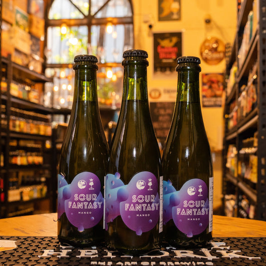 Botella de La Juguetes Perdidos Sour Fantasy Mango, una Sour Ale de la cervecería argentina Juguetes Perdidos. Con un ABV de 5.5%, esta cerveza refrescante ofrece aromas de mango fresco y notas cítricas. Su sabor es ácido, con una dulzura frutal y un final refrescante. Ideal para maridar con ensaladas, ceviches y postres frutales. El diseño de la botella refleja su estilo vibrante y veraniego.