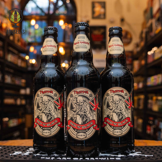 Botella de Trooper Red 'N' Black, una porter de edición limitada creada por Iron Maiden en colaboración con Robinsons Brewery. La etiqueta muestra a la mascota de la banda, Eddie, con detalles rojos y negros. ABV de 6.8%. Sabor a maltas tostadas, caramelo y un toque de miel. Ideal para acompañar carnes asadas y postres de chocolate. El diseño refleja la estética de Iron Maiden y su legado musical.