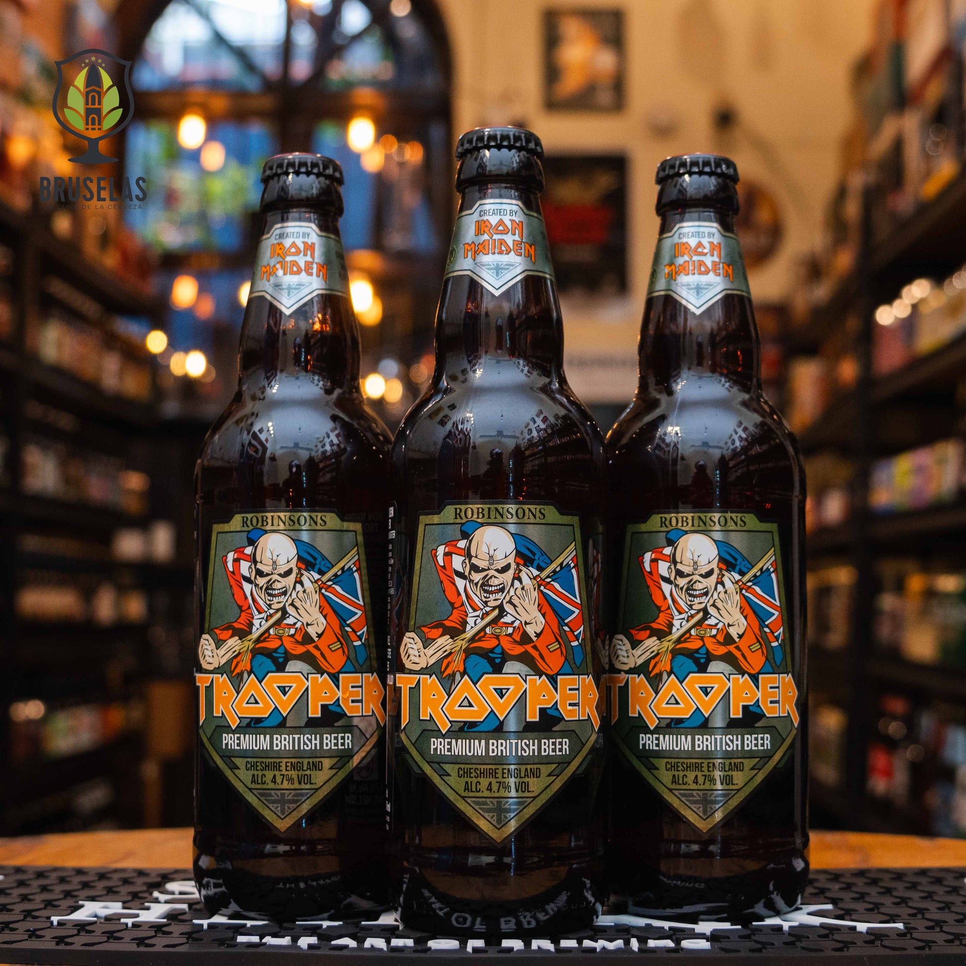 Botella de Trooper Premium British Beer, una ale británica creada por Iron Maiden y Robinsons Brewery. La etiqueta presenta a la mascota Eddie con la bandera británica. ABV de 4.7%. Sabor equilibrado entre notas cítricas, caramelo y un amargor moderado. Ideal para acompañar carnes asadas y hamburguesas. El diseño refleja la energía y estilo característicos de Iron Maiden.