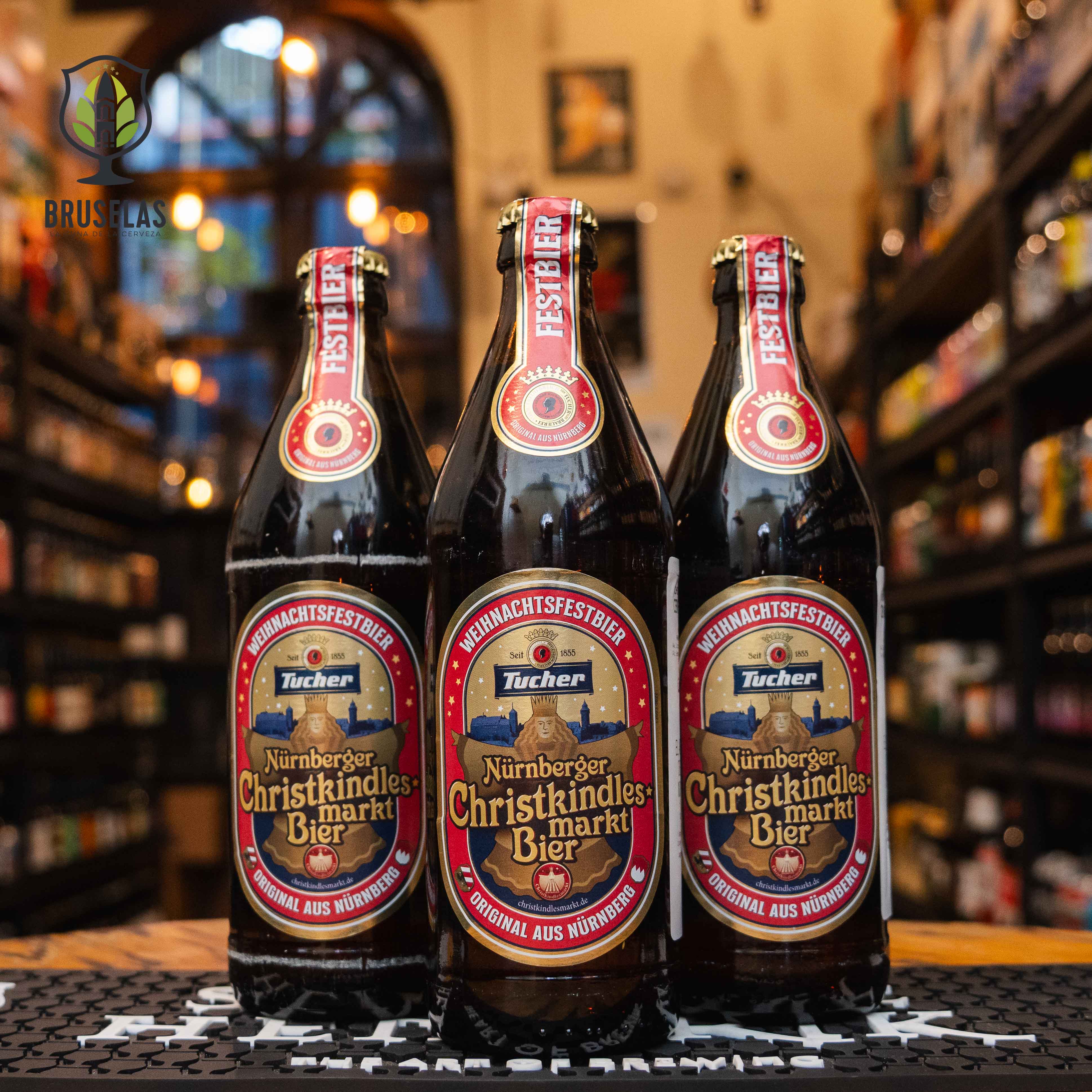 Botella de Tucher Christkindlesmarkt Bier, una Weihnachtsfestbier alemana de 5.5% ABV elaborada por Tucher Bräu para el mercado navideño de Núremberg. La etiqueta festiva destaca en rojo y dorado, evocando la temporada invernal. Con un perfil maltoso y ligeramente dulce, presenta notas de caramelo y un toque especiado, ideal para maridar con salchichas alemanas, pretzels y carnes asadas.