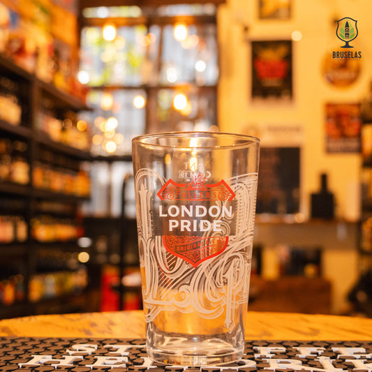 Vaso London Pride 500ml, de cristal tipo pinta inglesa con logo rojo y blanco, ubicado sobre una barra en un ambiente cervecero. Su diseño clásico resalta su uso ideal para ales británicas tradicionales.