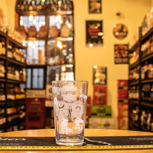 Vaso Marston’s 400ml, de cristal tipo pinta con logo y detalles gráficos en blanco. Ubicado sobre una barra en un ambiente cervecero, resaltando su uso ideal para ales británicas.