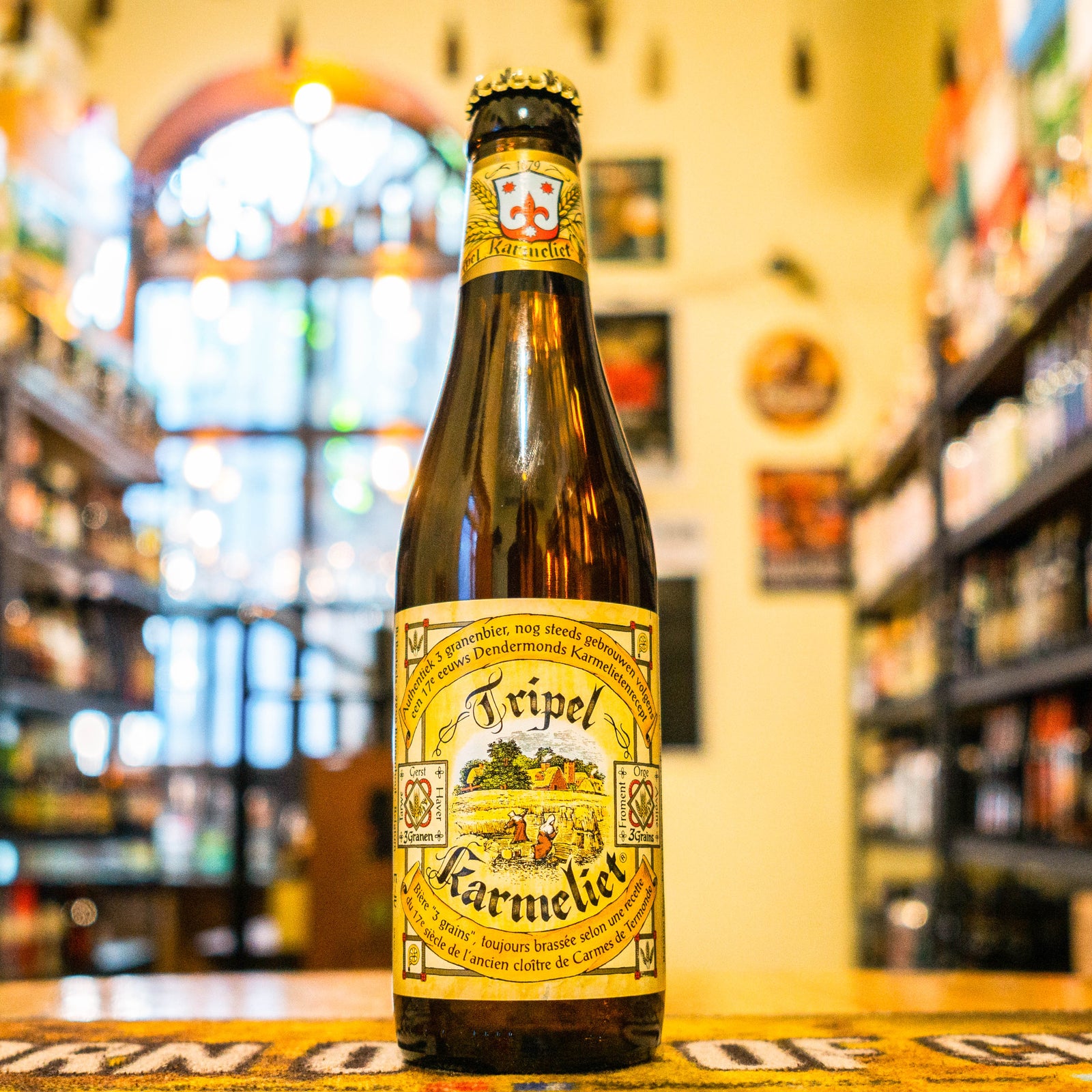Botella de Tripel Karmeliet 330 ml sobre barra de madera, fondo de tienda de cervezas artesanales belgas