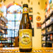 Botella de Tripel Karmeliet 330 ml sobre barra de madera, fondo de tienda de cervezas artesanales belgas